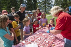 A woman in a red shirt volunteering for Canada Day hands out Canada Day themed cupcakes to children